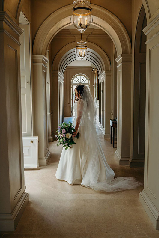 Bride standing in arched corridor holding wedding bouquet